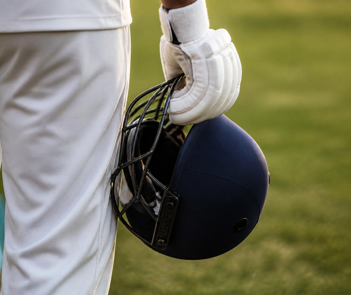Cricketer holding a navy batting helmet at their side on the outfield